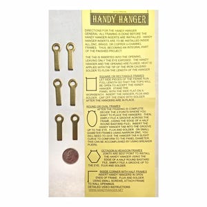 May include: A set of brass-colored Handy Hanger inserts for picture frames, with instructions on a yellow card. The inserts have a keyhole shape and are designed to be soldered into frames. A penny is included for size reference.