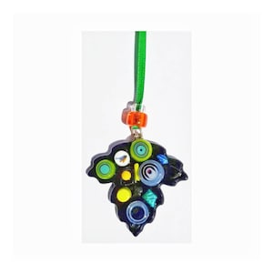 May include: A black glass pendant shaped like a leaf with colorful glass mosaic details, including circles, squares, and a small bird. The pendant is attached to a green ribbon.