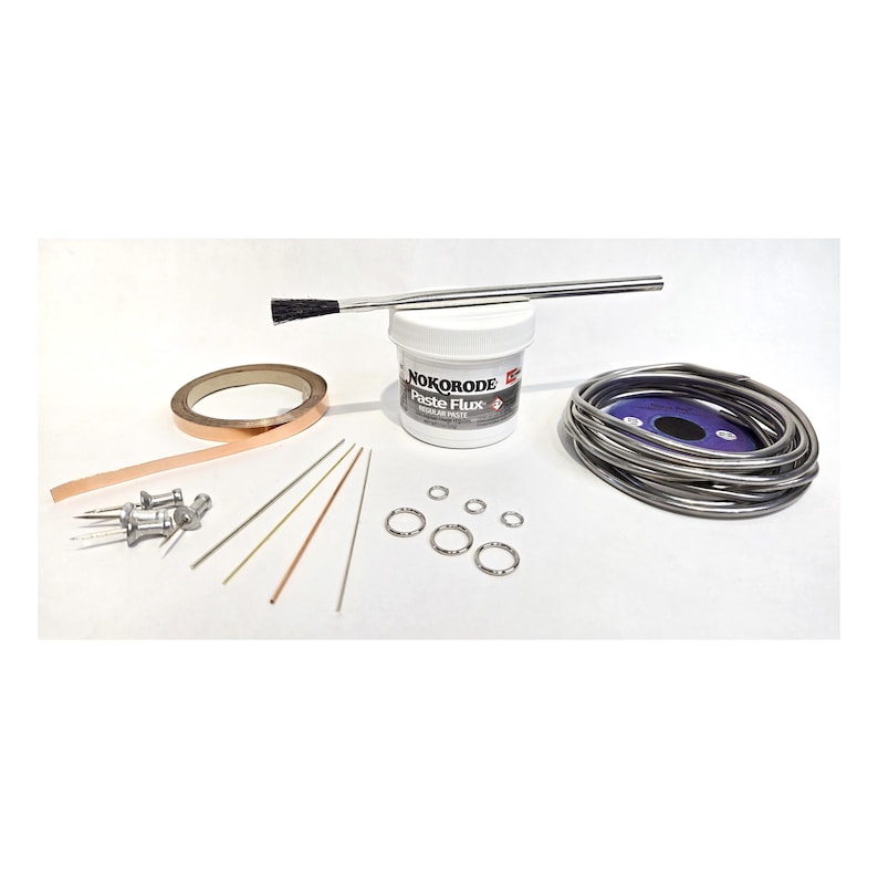 Puede incluir: Un kit de soldadura que contiene un recipiente blanco de pasta de fundente Nokorode, un cepillo de metal, un rollo de cinta de cobre, una bobina de hilo de soldar plateado, cuatro pasadores de metal, cuatro varillas finas y tres anillas plateadas.