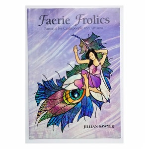 May include: A book titled "Faerie Frolics: Patterns for Craftspeople and Artisans" by Jillian Sawyer. The cover features a colorful illustration of a fairy sitting on a large iridescent peacock feather.