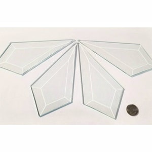 May include: Five clear glass diamond-shaped pieces, each with a beveled edge, arranged in a starburst pattern. A US quarter is included for scale.