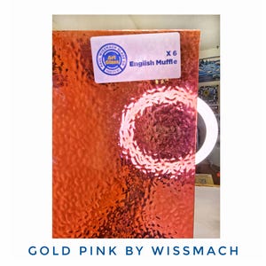 May include: Gold and pink textured glass sheet with a label that reads "Wissmach Glass Co." and "English Muffle". The sheet has a bubbly texture and is labeled "X 6". The text "Gold Pink by Wissmach" is at the bottom.