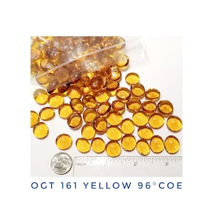 May include: A close-up of a pile of yellow glass beads. The beads are about 1/2 inch in diameter and have a smooth, shiny finish. A ruler is in the image for scale. The text "OGT 161 YELLOW 96°COE" is visible in the image.