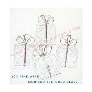 May include: Four clear glass squares with a textured pattern, each wrapped in pink wire to resemble a gift box with a bow. 20G Pink Wire Morisco Textured Glass.