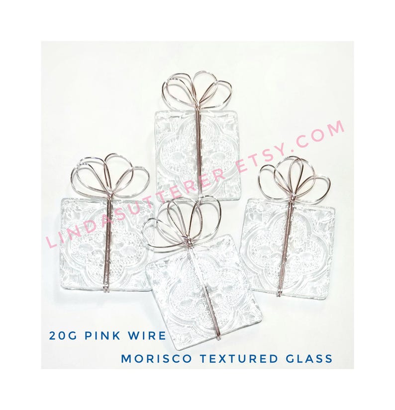 May include: Four clear glass squares with a textured pattern, each wrapped in pink wire to resemble a gift box with a bow. 20G Pink Wire Morisco Textured Glass.