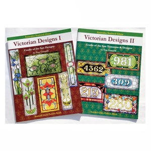 May include: Two books titled "Victorian Designs I" and "Victorian Designs II" by Dan Gamaldi. Both books feature stained glass patterns and designs. The first book has a maroon cover and the second book has a green cover.