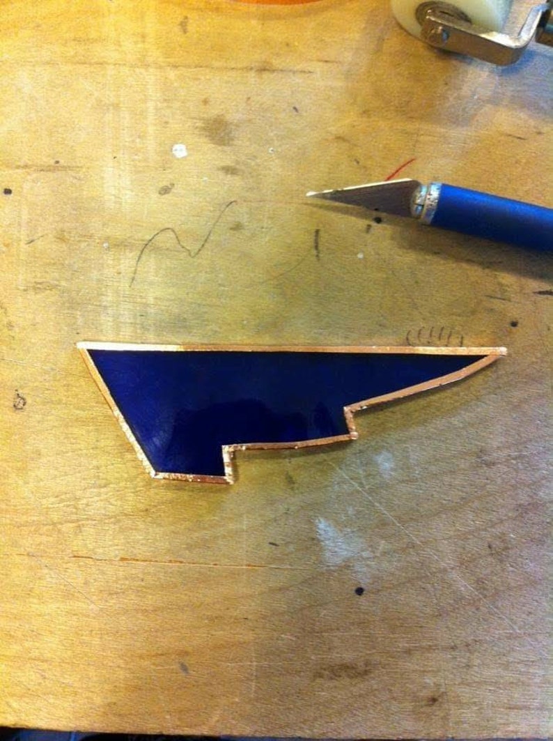 May include: A dark blue glass piece with a gold border, shaped like a wing, on a wooden surface.