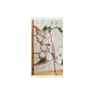 May include: Close-up of a stained glass piece being assembled. White glass flowers with yellow centers are being joined with copper foil tape. The text "FUSED PINK CENTERS ARE RAISED UP WITH CARDBOARD" and "I CUT THE FOIL NARROW FOR SMALL PIECES" are visible.