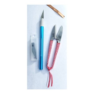 May include: A blue craft knife with a replaceable blade and a red and white striped pair of small scissors with a white and red tassel.