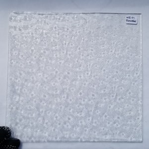 May include: A clear glass sheet with a textured surface featuring a repeating pattern of small, star-shaped designs. The sheet has a label in the top right corner that reads "WI 01 Floratac".