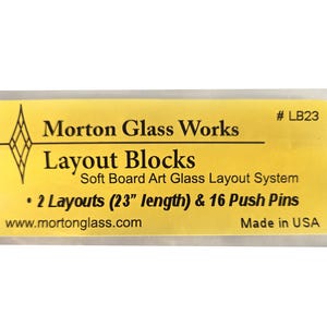May include: Yellow label with black text that reads "# LB23 Morton Glass Works Layout Blocks Soft Board Art Glass Layout System • 2 Layouts (23" length) & 16 Push Pins www.mortonglass.com Made in USA"