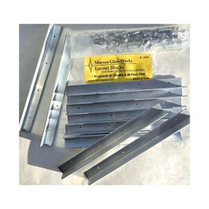 May include: A set of 10 silver metal layout blocks for glass art, with 40 push pins. The blocks are 6 inches long and are packaged in a clear plastic bag. The package label reads "Morton Glass Works Layout Blocks Soft Board Art Glass Layout System 10 Layouts (6 length) & 40 Push Pins www.mortonglass.com Made in USA #LB06".
