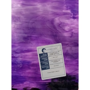 May include: A sheet of Oceanside Glass & Tile in shades of purple, with a marbled appearance. A white label in the lower right corner displays product information, including the product code 444-1W-F and the name "Deep Violet Pale Purple Watergato."