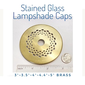 May include: A circular brass stained glass lampshade cap featuring a central hole and a decorative lattice cutout pattern. A ruler is positioned below the cap, showing a diameter of approximately 3 inches, alongside a US dime for scale.