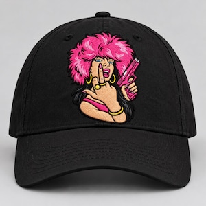 Puede incluir: Una gorra de béisbol negra con un parche bordado de una persona con cabello rosa brillante, que usa aros y anillos dorados, sostiene una pistola rosa mientras hace un gesto con el dedo medio. El diseño utiliza colores y contornos llamativos.