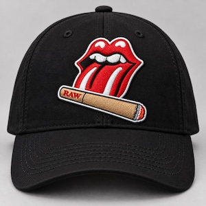 Könnte beinhalten: Eine schwarze Baseballkappe mit einem gestickten Aufnäher auf der Vorderseite. Der Aufnäher zeigt einen rot-weißen Mund mit herausgestreckter Zunge über einer beigen, gedrehten Zigarette mit dem roten Schriftzug RAW darauf.
