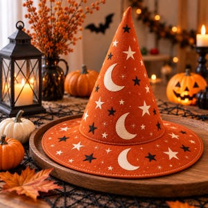May include: A pointed orange witch hat featuring a pattern of white crescent moons and both white and black stars. The hat has a wide, flat brim and a tall, conical crown, constructed from a felt-like material with visible stitching along the brim edge.