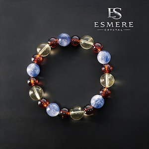 Peut inclure: Un bracelet composé de perles sphériques polies alternant entre le bleu clair translucide, l'ambre profond et le jaune transparent. Le texte ESMERE CRYSTAL est visible dans le coin supérieur droit sur un fond sombre.