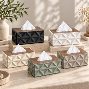 Puede incluir: Cinco cajas rectangulares para pañuelos con tapa de madera oscura y un patrón lateral geométrico facetado. Las cajas vienen en negro, blanco, crema, verde salvia y gris claro, cada una con un pañuelo blanco asomando por la ranura central.