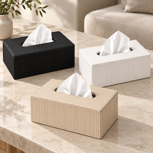 May include: Three rectangular tissue box covers in black, white, and beige. Each cover features a vertical ribbed texture on the sides, a smooth top surface, and a central oval opening with a white tissue protruding from the top of each unit.