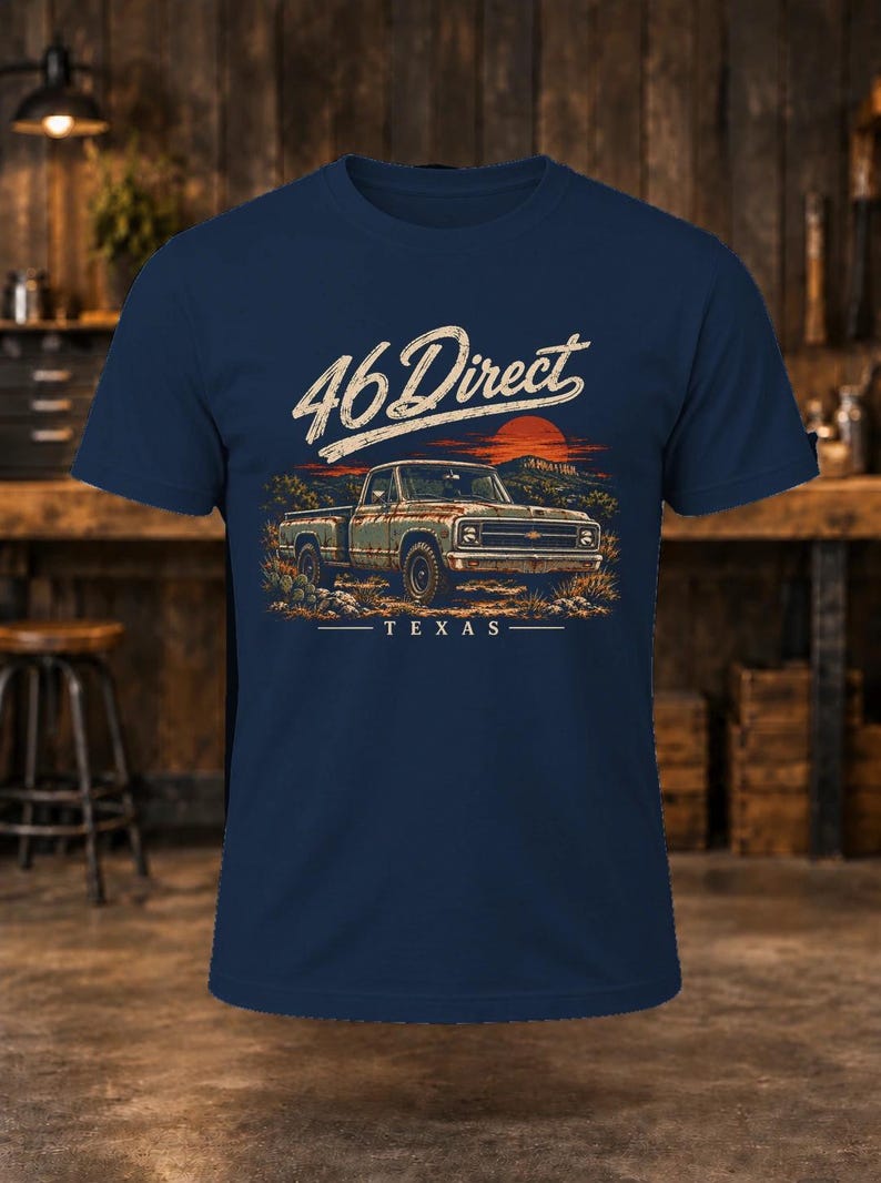 K&ouml;nnte beinhalten: Ein marineblaues Kurzarm-T-Shirt mit einer Grafik eines alten Pick-ups in einer W&uuml;stenlandschaft bei Sonnenuntergang. Der Text 46 Direct ist in wei&szlig;er Schreibschrift &uuml;ber dem Fahrzeug gedruckt, darunter steht das Wort TEXAS.