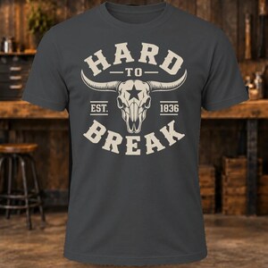 May include: A charcoal gray short-sleeve t-shirt featuring a cream-colored graphic of a longhorn skull with a star on the forehead. The text reads HARD TO BREAK and EST. 1836 in a bold, arched font surrounding the central skull illustration.