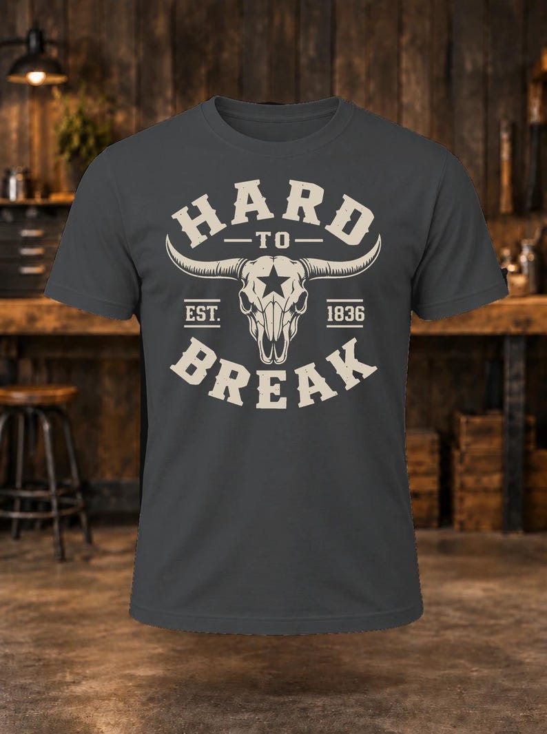 May include: A charcoal gray short-sleeve t-shirt featuring a cream-colored graphic of a longhorn skull with a star on the forehead. The text reads HARD TO BREAK and EST. 1836 in a bold, arched font surrounding the central skull illustration.