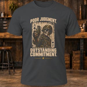 Puede incluir: Una camiseta gris carb&oacute;n con un gr&aacute;fico de un soldado esqueleto con casco sosteniendo una granada, sobre un fondo de carta de as de picas. El texto dice POOR JUDGMENT en la parte superior y OUTSTANDING COMMITMENT en la parte inferior.