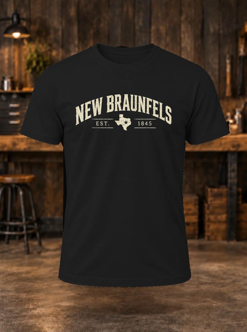 May include: A black short-sleeve t-shirt featuring the text NEW BRAUNFELS in a distressed cream font. Below the text is the abbreviation EST. and the year 1845, separated by a white silhouette of the state of Texas with a star.