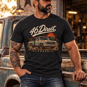 K&ouml;nnte beinhalten: Ein schwarzes Kurzarm-T-Shirt mit einem Grafikdruck eines alten Pick-up-Trucks in einer W&uuml;stenlandschaft bei Sonnenuntergang. Der Text 46 Direct ist in Schreibschrift &uuml;ber dem Truck und das Wort TEXAS darunter aufgedruckt.