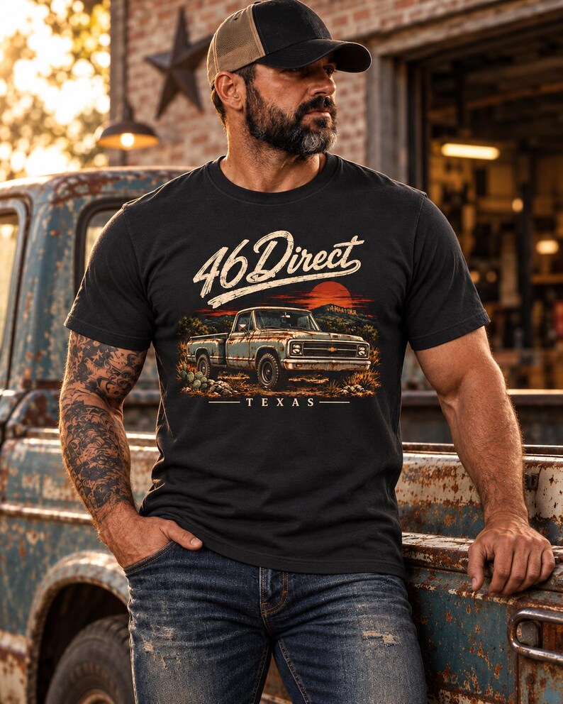 K&ouml;nnte beinhalten: Ein schwarzes Kurzarm-T-Shirt mit einem Grafikdruck eines alten Pick-up-Trucks in einer W&uuml;stenlandschaft bei Sonnenuntergang. Der Text 46 Direct ist in Schreibschrift &uuml;ber dem Truck und das Wort TEXAS darunter aufgedruckt.