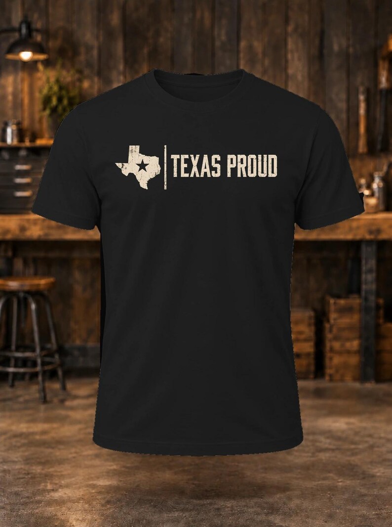 May include: A black short-sleeved t-shirt featuring a distressed white graphic of the state of Texas with a star inside, followed by a vertical line and the text "TEXAS PROUD" in a distressed white sans-serif font across the chest.