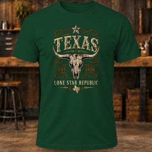 May include: A dark green short-sleeve t-shirt featuring a graphic print of a longhorn skull centred above the text TEXAS, EST. 1836, and LONE STAR REPUBLIC, with a small star icon at the top and a small map of Texas at the bottom.