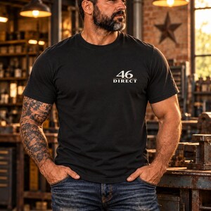 May include: A black short-sleeved crew neck t-shirt featuring the text 46 DIRECT printed in white on the upper left chest area. The shirt is paired with blue denim jeans that have a distressed finish and visible wear along the pockets.