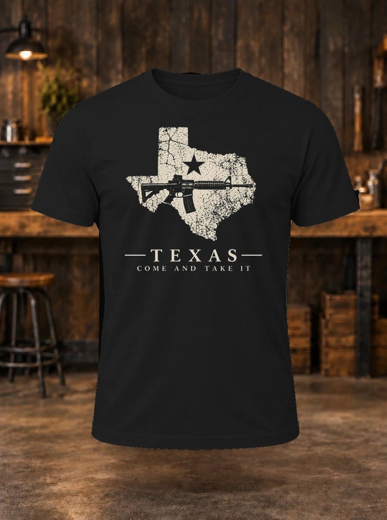 May include: A black short-sleeve t-shirt featuring a distressed white graphic of the state of Texas with a black star and a rifle silhouette. Below the graphic, the text reads: TEXAS COME AND TAKE IT in white capital letters.