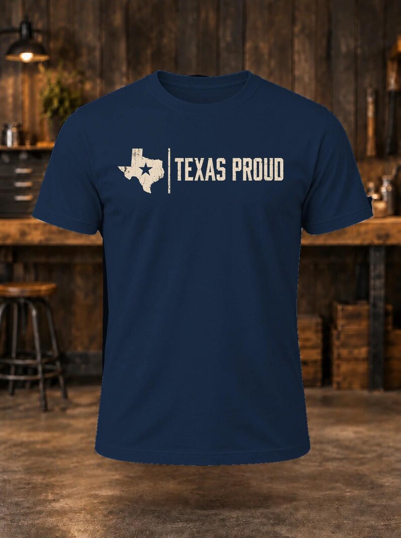 May include: A navy blue short-sleeve t-shirt featuring a distressed white graphic of the state of Texas with a star inside, followed by a vertical line and the text "TEXAS PROUD" in a bold, distressed white sans-serif font.