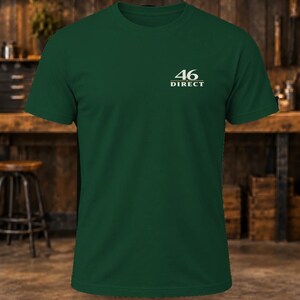 May include: A dark green short-sleeve t-shirt featuring a crew neckline. On the upper left chest, there is a white graphic print that displays the number 46 above the word DIRECT, with a horizontal line separating the two elements.