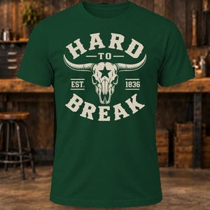 May include: A dark green short-sleeve t-shirt featuring a cream-colored graphic of a longhorn skull with a star on the forehead. The text reads HARD TO BREAK with EST. 1836 on either side of the skull, centered on the chest of the garment.