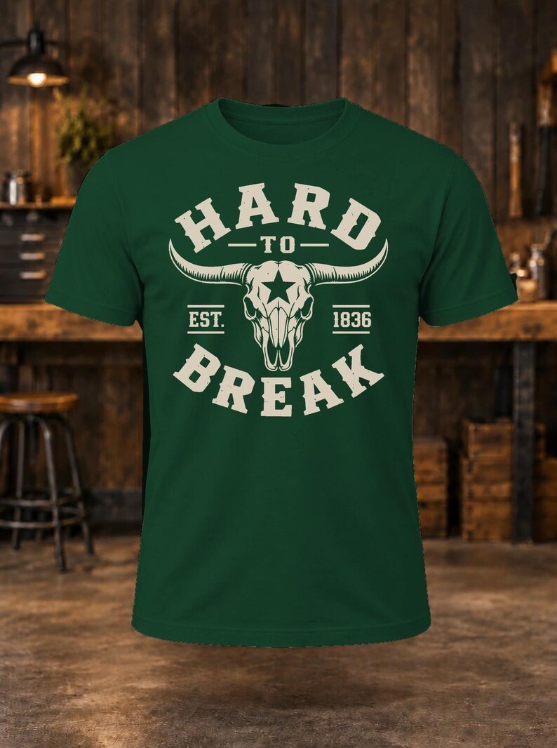 May include: A dark green short-sleeve t-shirt featuring a cream-colored graphic of a longhorn skull with a star on the forehead. The text reads HARD TO BREAK with EST. 1836 on either side of the skull, centered on the chest of the garment.