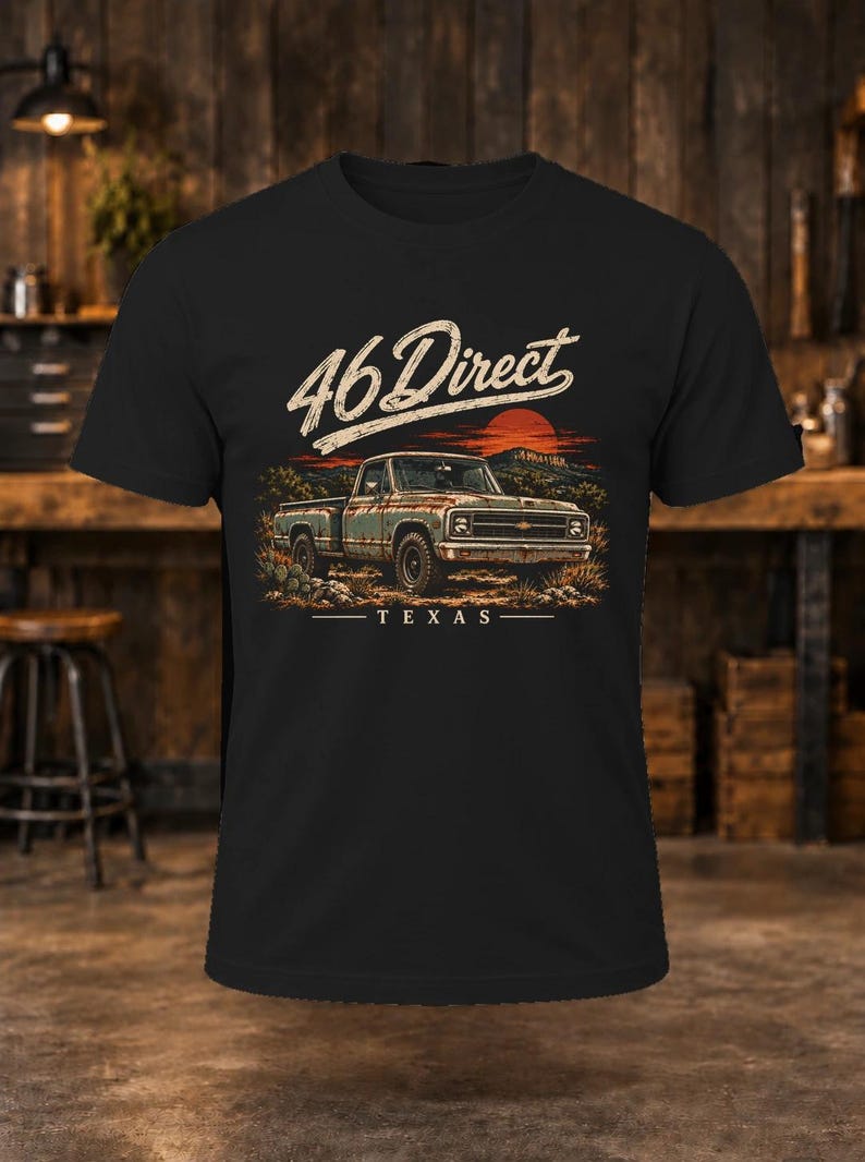 K&ouml;nnte beinhalten: Ein schwarzes T-Shirt mit einem Grafikdruck eines alten Pick-up-Trucks in einer W&uuml;stenlandschaft bei Sonnenuntergang. Der Text 46 Direct steht &uuml;ber dem Truck und das Wort TEXAS ist darunter in wei&szlig;er Schrift gedruckt.