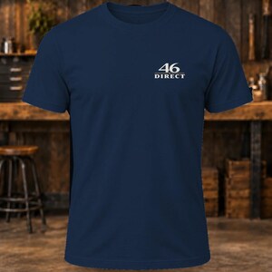 May include: A navy blue short-sleeve t-shirt featuring the white text 46 DIRECT printed on the upper left chest area. The shirt has a crew neckline and a standard fit, constructed from a solid-colored fabric with a clean, simple design.
