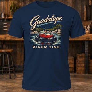 May include: A navy blue short-sleeve t-shirt featuring a graphic of a red and white cooler sitting on a black inner tube in a river. The text Guadalupe is printed in a cream script above, and RIVER TIME is printed in cream block letters below.