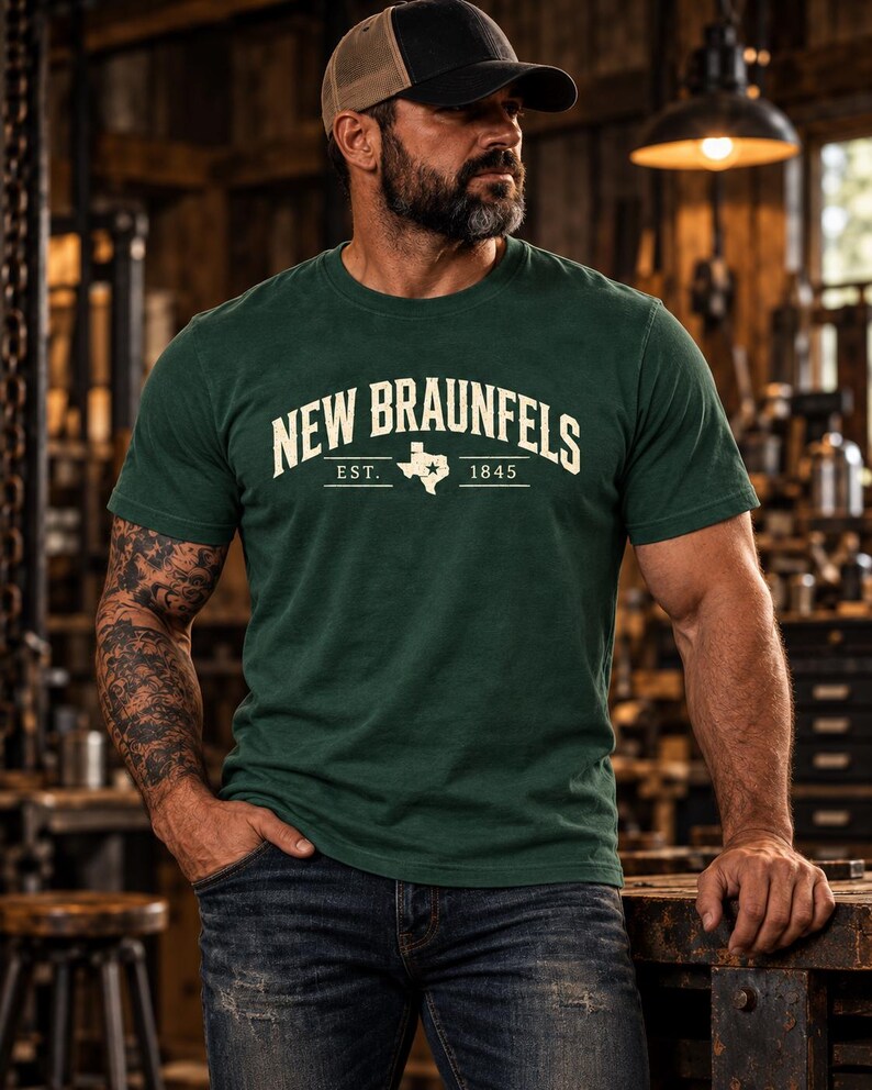 May include: A dark green short-sleeve t-shirt featuring the text NEW BRAUNFELS in a cream-colored arched font, with the abbreviation EST. 1845 and a graphic outline of the state of Texas with a star located in the center of the chest.