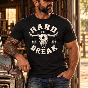 May include: A black short-sleeve t-shirt featuring a white graphic of a longhorn skull with a star on the forehead. The text reads HARD TO BREAK with EST. 1836 printed below the skull. The design is centered on the chest of the garment.