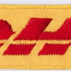 Puede incluir: Un parche rectangular bordado con fondo amarillo y el texto rojo DHL centrado. El diseño incluye tres líneas rojas horizontales a ambos lados de las letras, todo ello encerrado dentro de un borde cosido de color amarillo.