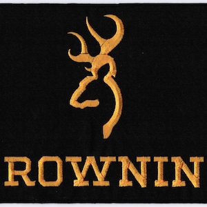 May include: A rectangular black patch featuring an embroidered gold-colored Browning buckmark logo at the top center. Below the logo, the word BROWNING is embroidered in a bold, gold-colored serif font across the bottom of the patch.