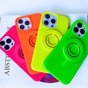 May include: Four phone cases in bright neon colors: green, yellow, orange, and pink. Each case has a raised ring on the back for a secure grip.