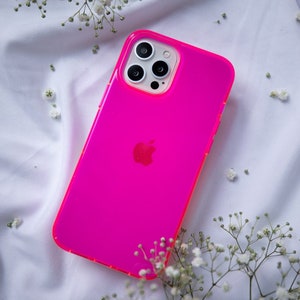 May include: A bright pink phone case with a clear back and a black Apple logo. The case has a raised camera bump with three black camera lenses.