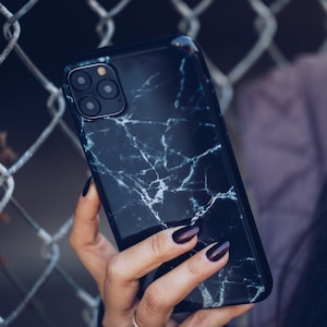 May include: A black phone case with a white marble pattern. The case has a camera lens cutout and a black border.