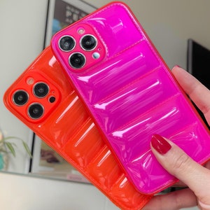Puede incluir: Dos fundas para iPhone en rosa brillante y naranja con un diseño acolchado. Las fundas están hechas de un material brillante y gomoso.